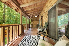 A wooden cabin with a porch, a large window, and a view of the forest. - Brownstone Lodge – Private 55-Acre Retreat with Hot Tub & Fire Pit (Jeffersonville)