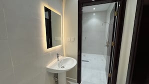 Un baño moderno con un lavabo blanco, un espejo y una zona de ducha visible a través de una puerta abierta.