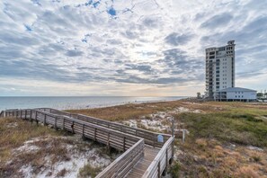 A beach with a wooden boardwalk leading to a building with multiple floors and balconies.
