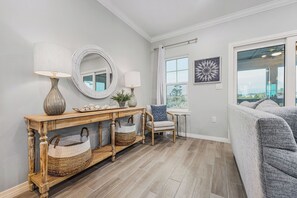 A living room with a console table, two lamps, a mirror, a window, a sofa, and a view of the outdoors.