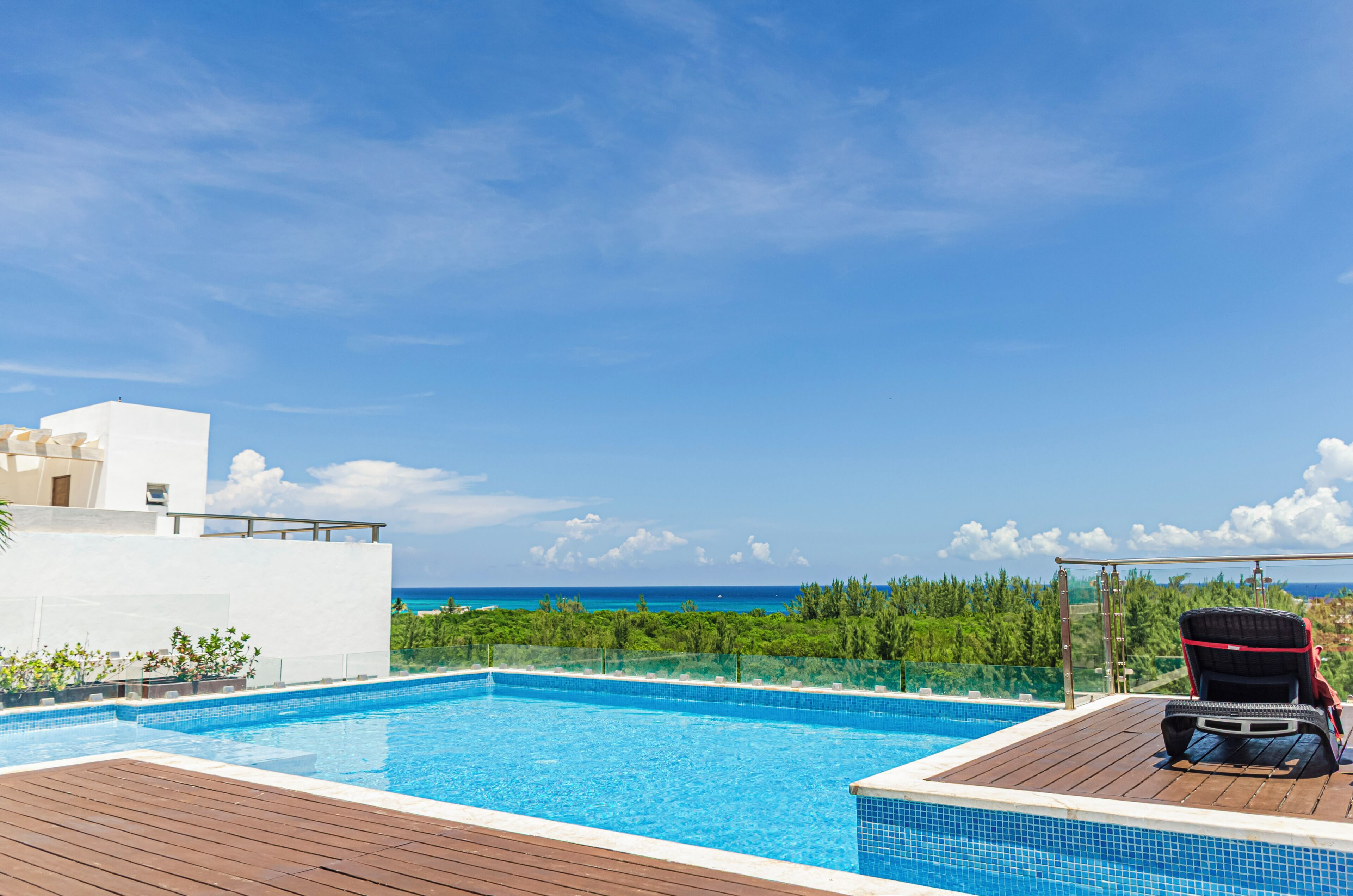 Une piscine avec une terrasse en bois et un fauteuil de relaxation, offrant une vue sur une plage et l’océan.