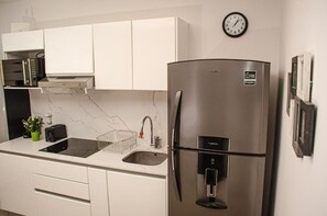 Una cocina moderna con un refrigerador de acero inoxidable, horno empotrado, un lavamanos y un reloj en la pared.
