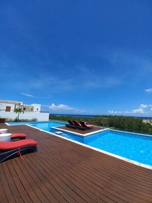 Una piscina en la azotea con cubierta de madera y sillones de descanso.
