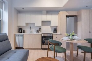 Eine moderne Küche mit Geschirrspüler, Herd und Spüle, ein Essbereich mit rundem Tisch und Stühlen sowie ein graues Sofa.