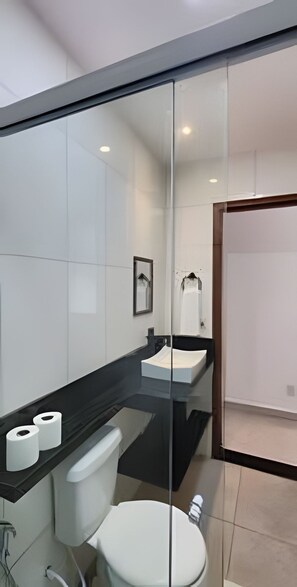 Um banheiro moderno com divisória de vidro, vaso sanitário branco, pia e espelho.