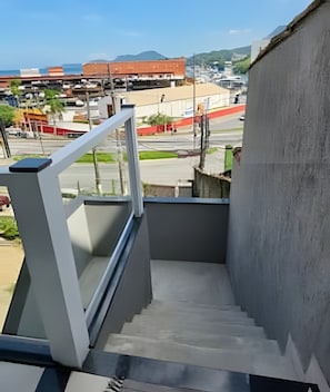 A concrete staircase with a metal handrail leading to a balcony overlooking a cityscape with buildings and a distant mountain. - Studio RD with Queen bed for couples 2 (Angra dos Reis)