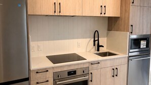 A modern kitchen with wooden cabinets, stainless steel appliances, a double sink, and a built-in oven. - Elegant 1+1bed 1bath |Sauna|Gym | Cold plunge (Toronto)