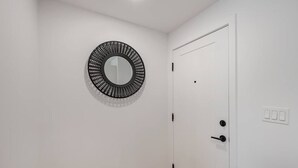 Une porte blanche avec une poignée noire, un mur blanc et un miroir rond doté d’un cadre noir.