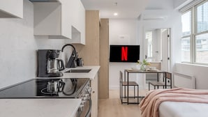 Une cuisine moderne avec un plan de travail noir, une machine à café et un téléviseur affichant le logo de Netflix.