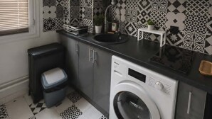 A compact kitchen with a washing machine, a microwave, and patterned tiles. - Charming Apt Steps from Eiffel Tower & Quai Branly (Paris)