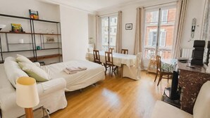 A cozy room with a bed, a dining table, chairs, a bookshelf, and a window with curtains. - Charming Apt Steps from Eiffel Tower & Quai Branly (Paris)