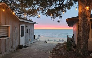 A wooden building with a door and windows, a bench, and a view of the ocean at sunset.