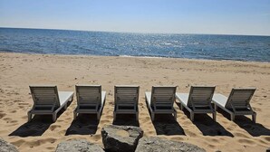 Uma praia com cinco cadeiras de praia alinhadas em fila, voltadas para o oceano.