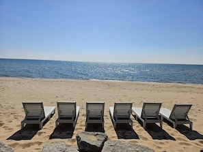 Ein Strand mit fünf Liegestühlen, die in einer Reihe zum Meer ausgerichtet sind.