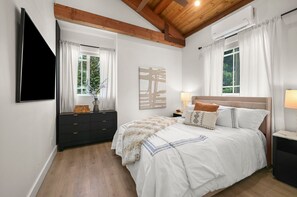 A bedroom with a bed, a dresser, a TV, and a window with curtains.