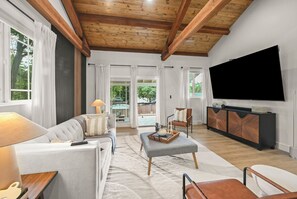 A modern living room with a sofa, ottoman, and a flat-screen TV mounted on the wall.