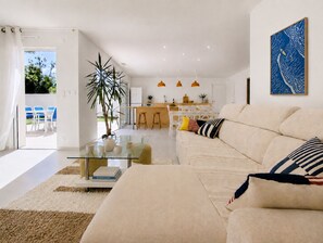 A modern living room with a sofa, a glass coffee table, and a dining area with chairs and a kitchen in the background. - Maison Terre Océan (Angles)