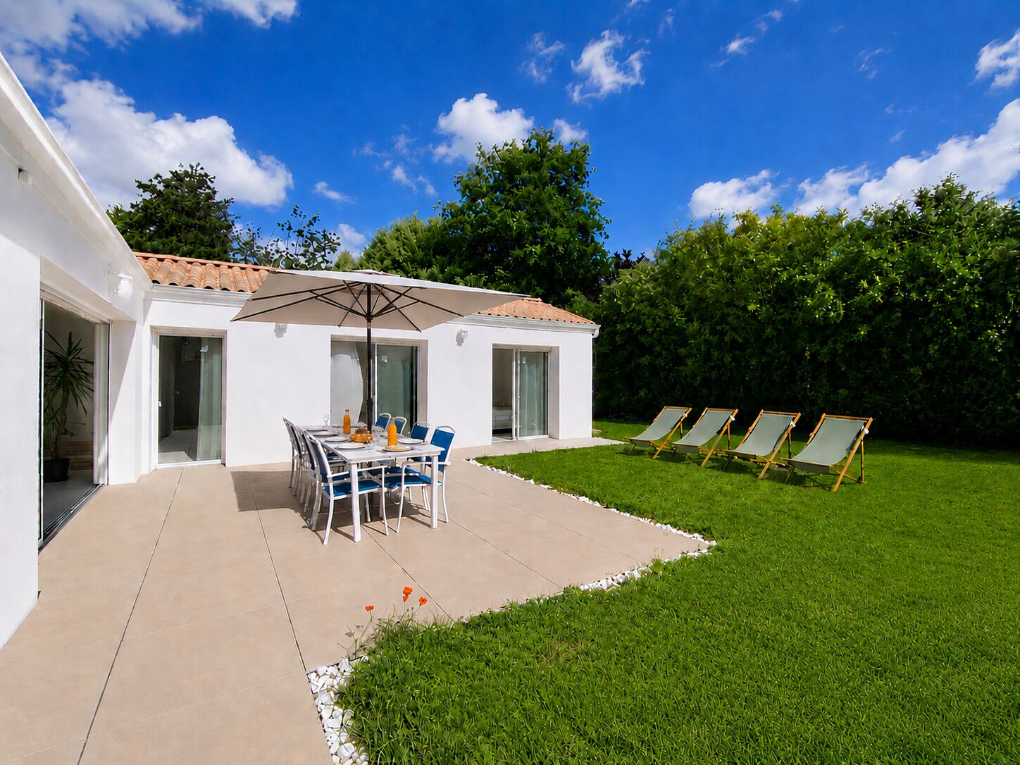 A modern house with a patio, a dining table with chairs, a covered outdoor area, and a lawn with sun loungers.