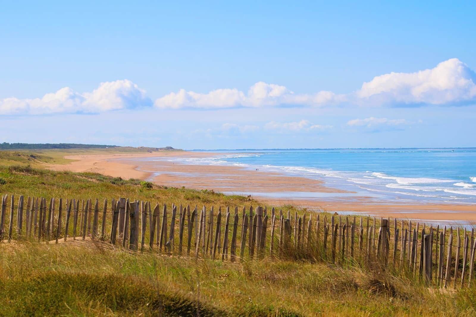 A beach with a wooden fence in the foreground and a clear sky.