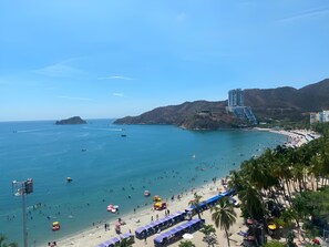 A beach with people, boats, and a large building. - Disfruta el Mar: Beachfront Apartment Steps from El Rodadero Beach (Gaira)