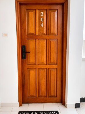 Eine Holztür mit der Nummer 304, einem schwarzen Klingelknopf und einem weiß gefliesten Boden.