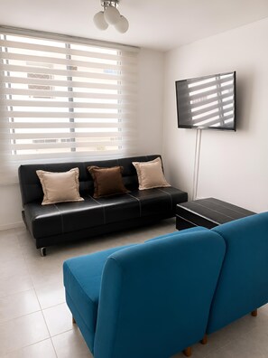Ein modernes Wohnzimmer mit einer schwarzen Couch, einem blauen Sessel und einem flachbildschirmfernseher an der Wand.