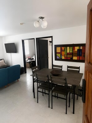 A dining area with a wooden table and chairs, a blue sofa, a TV, and a colorful abstract painting on the wall. - Disfruta el Mar: Beachfront Apartment Steps from El Rodadero Beach (Gaira)