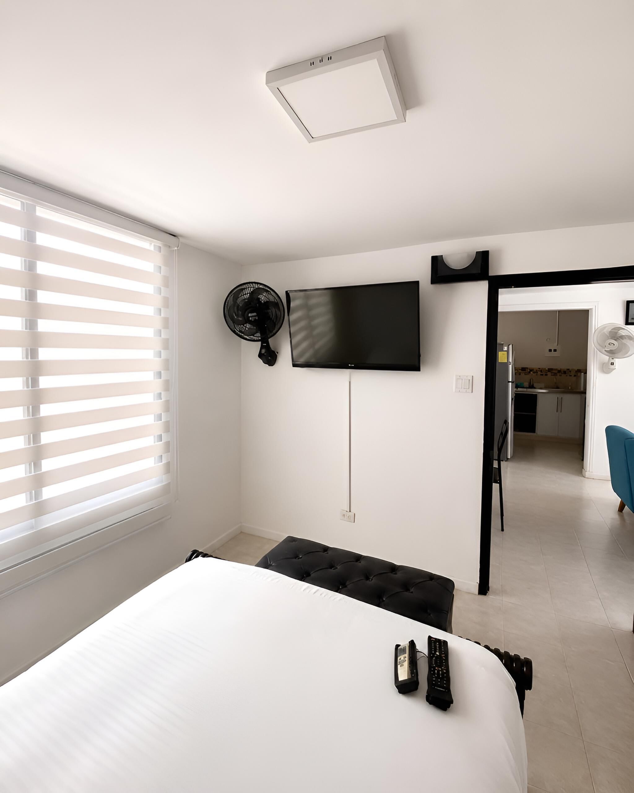 Ein Schlafzimmer mit einem Bett, einem Fernseher, einem Ventilator und einem Fenster mit Jalousien.