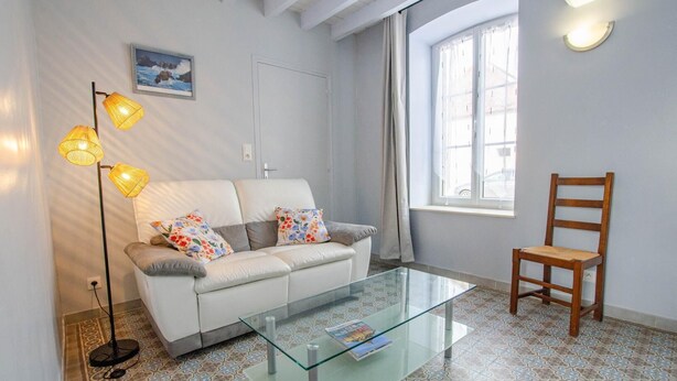 A living room with a sofa, a glass coffee table, a wooden chair, a floor lamp, and a window with curtains. - Le Nid d'Hirondelles (FONTAINE LES GRES)