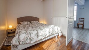A bedroom with a bed, nightstand, and a chair. - Le Nid d'Hirondelles (FONTAINE LES GRES)