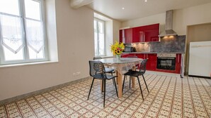 A kitchen with a dining table, chairs, a red cabinet, a stove, and a refrigerator. - Le Nid d'Hirondelles (FONTAINE LES GRES)