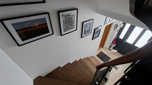 Uma escadaria com degraus de madeira e corrimão, que leva a um quarto com porta e janela.