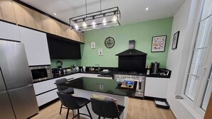 Cozinha moderna com ilha central, eletrodomésticos de aço inoxidável e parede verde decorativa.