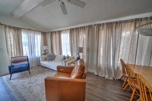 Un soggiorno con divano, poltrona, tavolo da pranzo e sedie, e una ventola a soffitto.