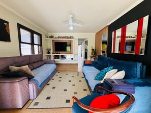 A living room with a sofa, a chair, a TV, and a ceiling fan. - Super house on the beach with pool, 60m from the sea, air conditioning, etc. (Guaratuba)