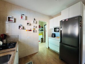 A kitchen with a refrigerator, microwave, and stove. There are cabinets and shelves with various items. - Super house on the beach with pool, 60m from the sea, air conditioning, etc. (Guaratuba)