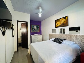 A bedroom with a bed, a ceiling fan, a painting, a mirror, and a door leading to another room. - Super house on the beach with pool, 60m from the sea, air conditioning, etc. (Guaratuba)