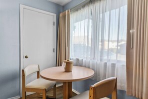 Een kamer met een ronde tafel, twee stoelen, een deur en een raam met dunne gordijnen.
