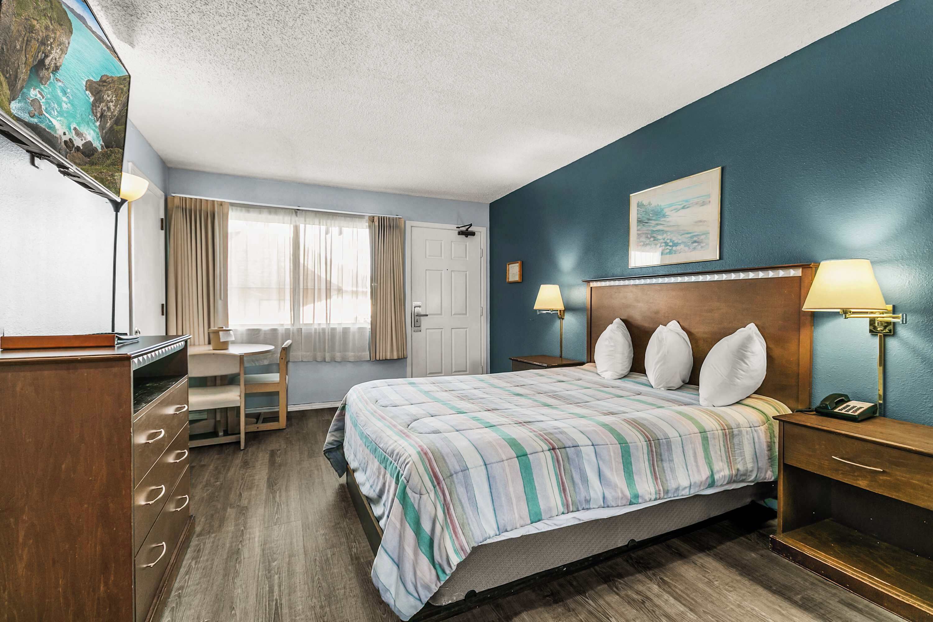 Une chambre d’hôtel avec un lit, des lampes de chevet, un bureau et une chaise.