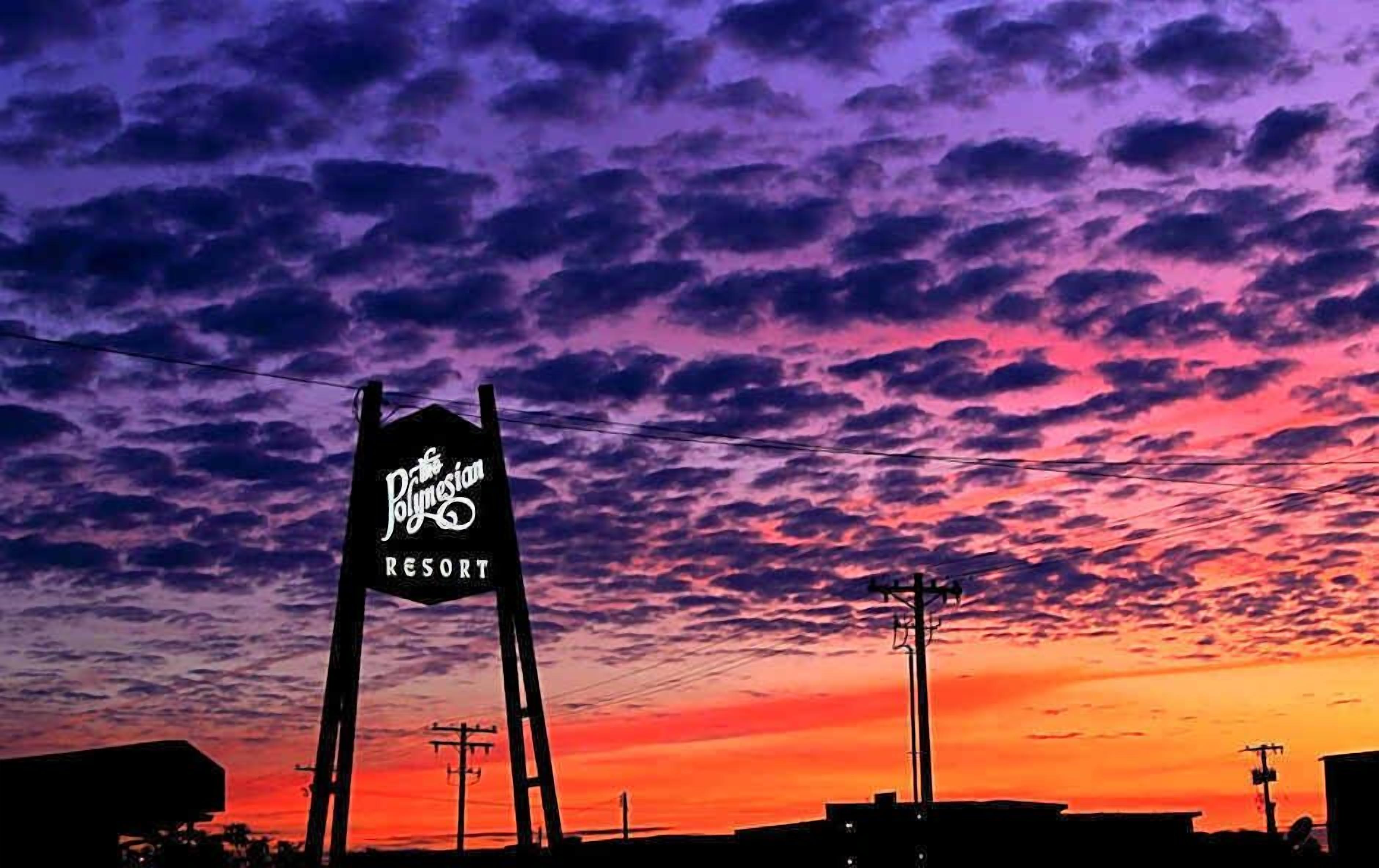 A sign for 'Polynesian Resort' against a sunset sky.
