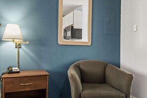 Ein Zimmer mit Nachttisch, Lampe, Stuhl, Spiegel und Thermostat an der Wand.