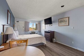 A bedroom with a bed, a desk, a chair, a TV, a dresser, and a window with curtains. - Ground Floor Studio - Kitchenette - Pet-Friendly! (Ocean Shores)