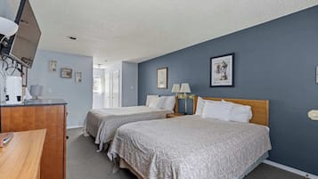 A hotel room with two beds, a desk, a TV, and a door leading to another room.