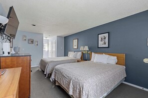 A hotel room with two beds, a desk, a TV, and a door leading to another room.
