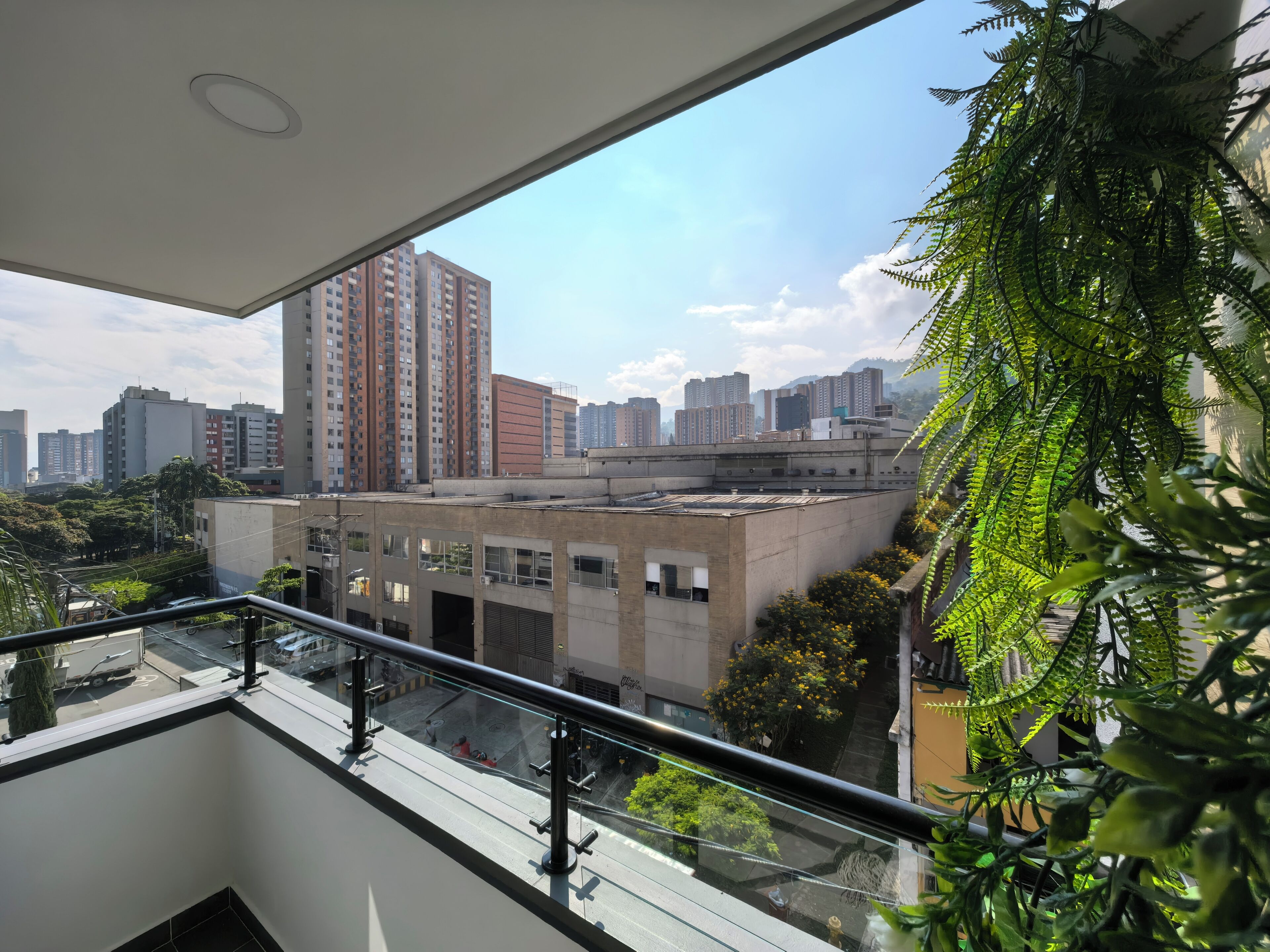A high-rise building with a balcony, a cityscape view, and a hanging plant.