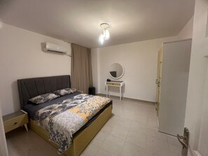 Une chambre à coucher comprenant un lit, une table de chevet, un appareil de climatisation, un miroir et une porte.