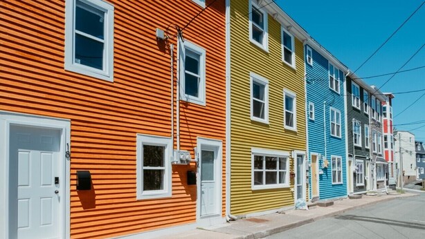 Een rij kleurrijke herenhuizen met witte deuren en ramen, een heldere lucht en een zichtbare straat.