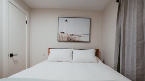 Een eenpersoonsbed met witte beddengoed, een hoofdbord, en een ingelijste foto van een vuurtoren aan de muur.