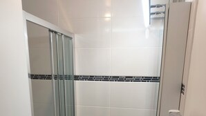 A bathroom with a glass shower enclosure, a sink with a wooden vanity, and a towel hanging on a rack. - 2 People | Near town center and beaches | Air-conditioned | Garden (Cavalaire sur Mer)