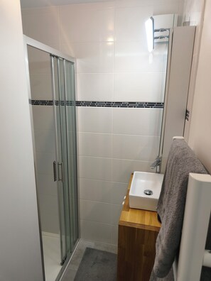 A bathroom with a glass shower enclosure, a sink with a wooden vanity, and a towel hanging on a rack. - 2 People | Near town center and beaches | Air-conditioned | Garden (Cavalaire sur Mer)